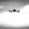 Sort/hvid billede af stor drone, der flyver i solnedgang.